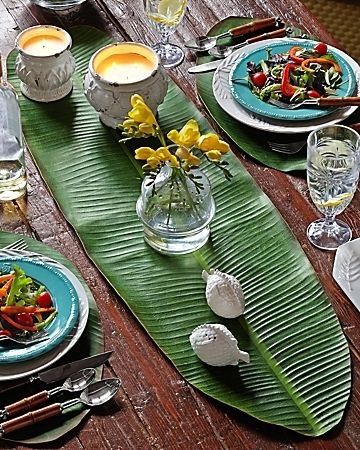 a wooden table topped with plates and bowls filled with food on top of green leaves