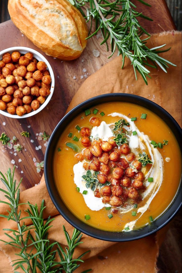 a bowl of carrot soup with garnishes and bread on the side next to it