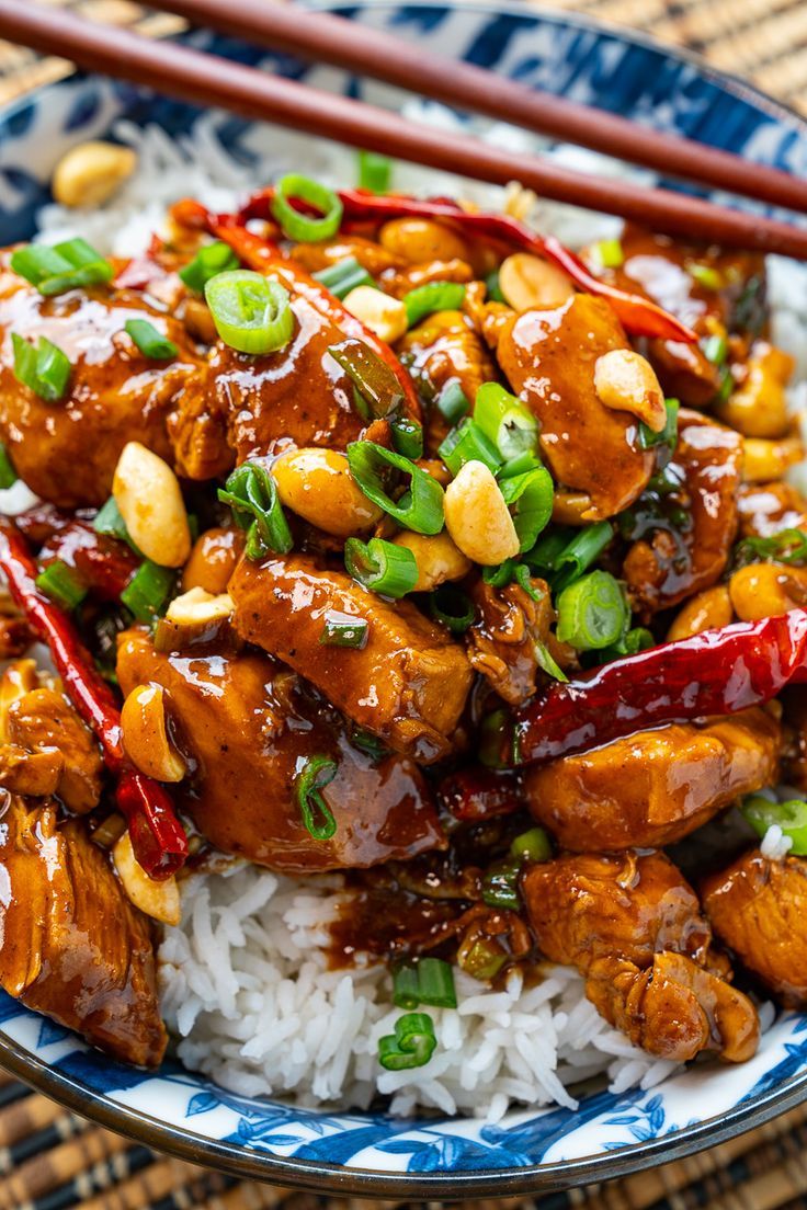 a blue and white plate topped with rice and meat covered in sauce, green onions and peanuts