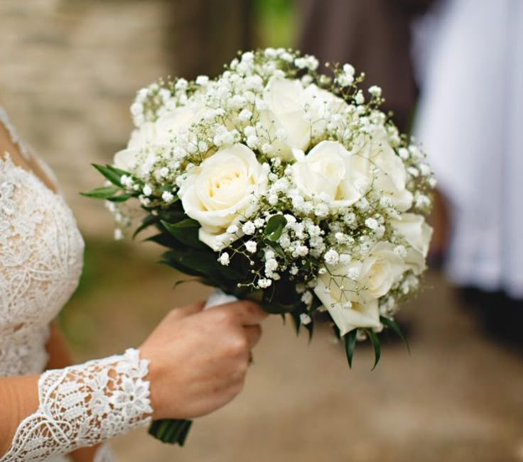 a bride holding a bouquet of white roses and baby's breath in her hand