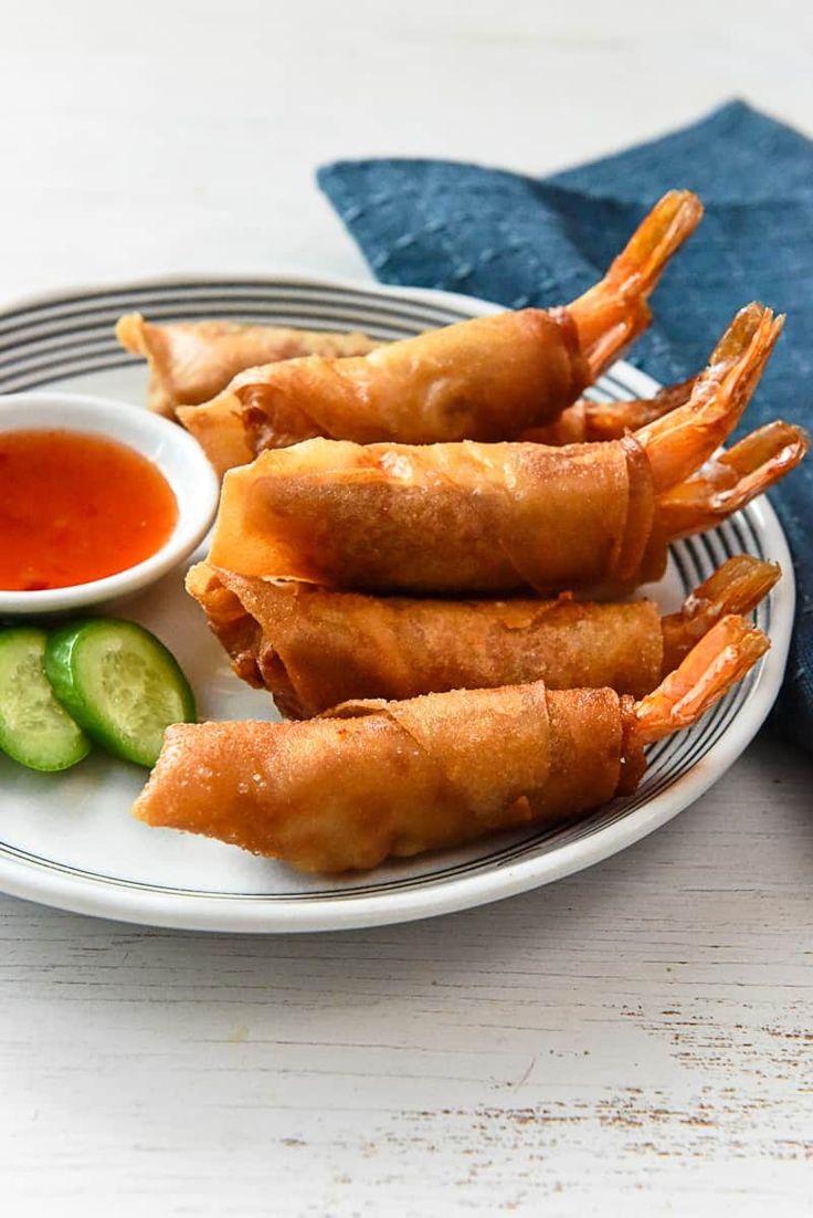 some shrimp sticks are on a plate with dipping sauce and cucumbers next to it