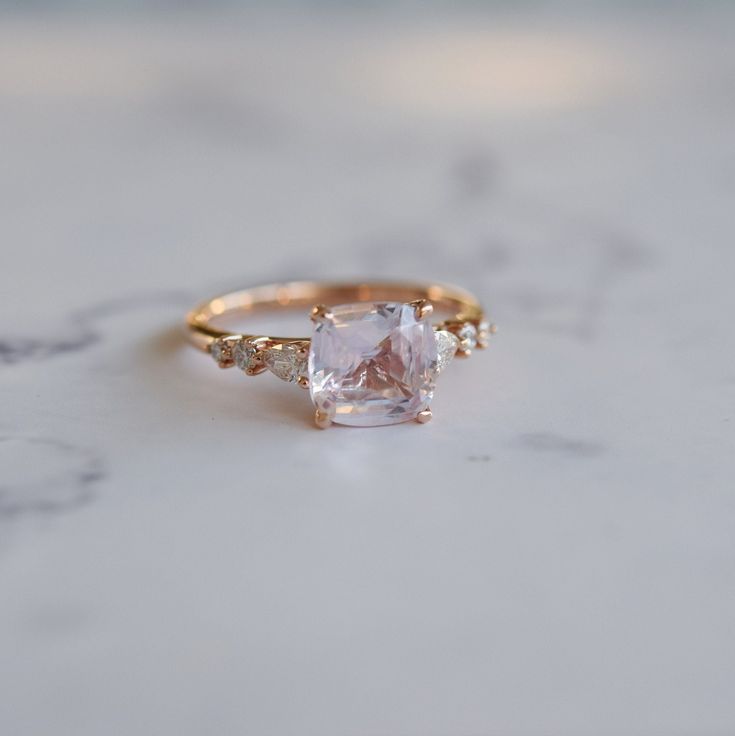 an engagement ring with a square cut diamond and three small diamonds around the band on a marble surface