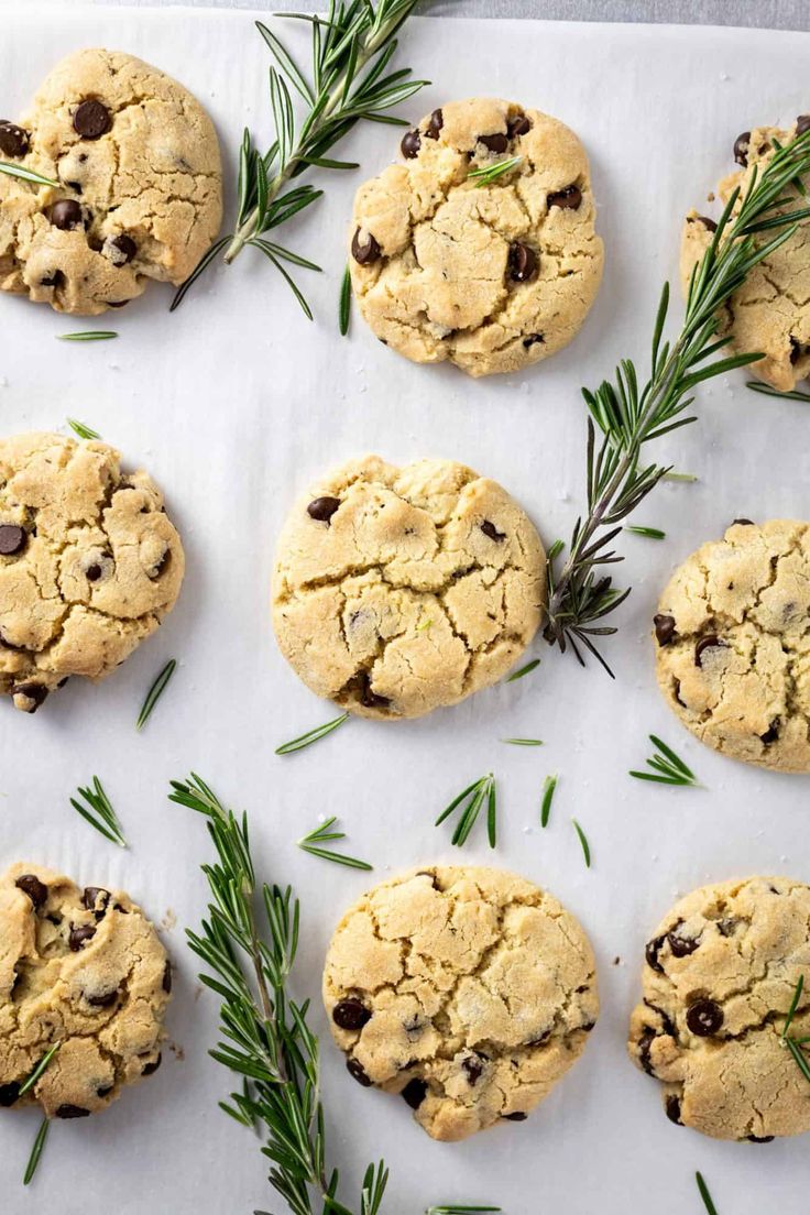 chocolate chip cookies and rosemary sprigs on a white paper lined baking sheet, ready to be eaten