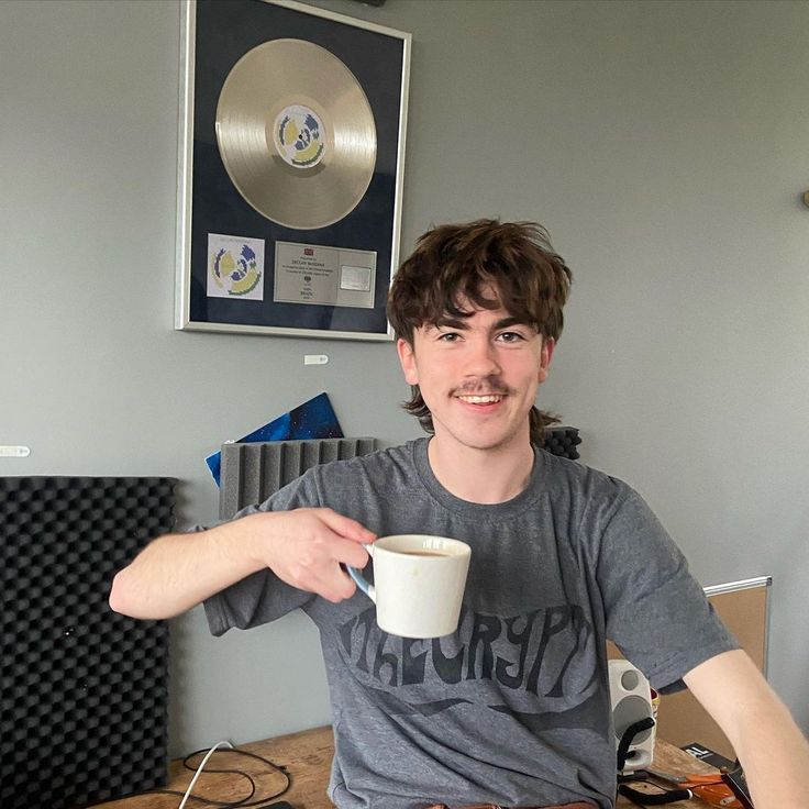 a young man sitting at a desk with a cup of coffee in front of him