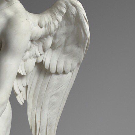 an angel statue with white wings on a gray background and the back side of it's body