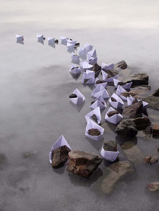 several origami boats floating on top of water next to rocks and pebbles in the sand