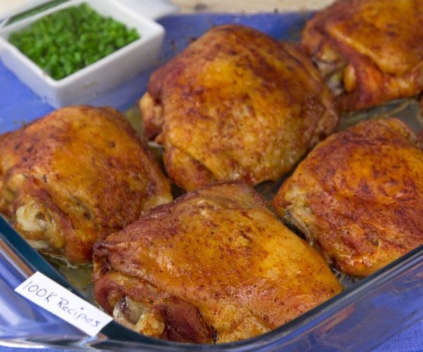 several cooked chicken in a glass dish with green peas and seasoning on the side