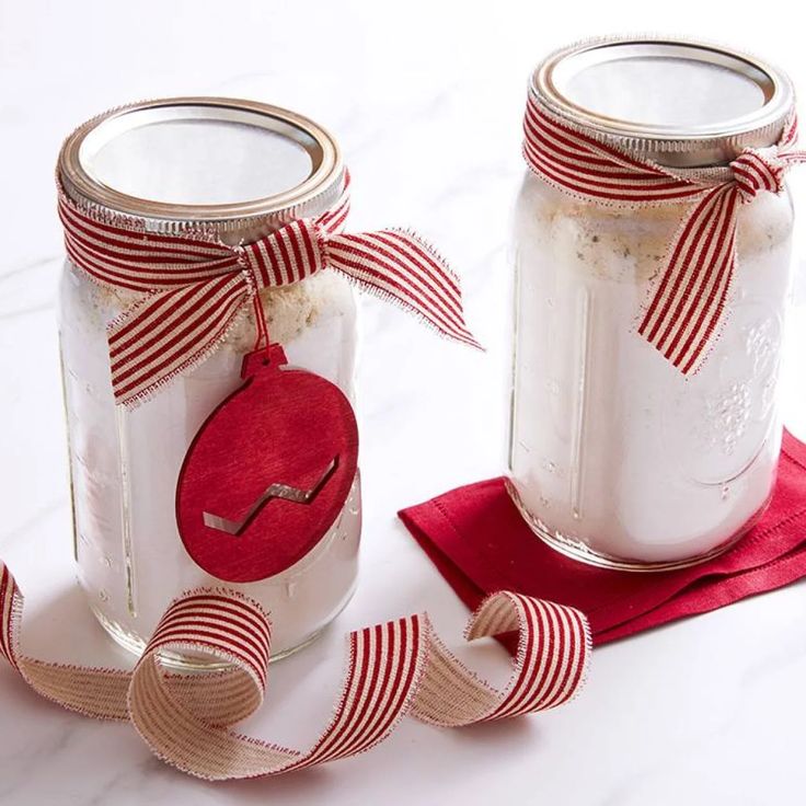 two mason jars decorated with red and white ribbon, one has an ornament on it