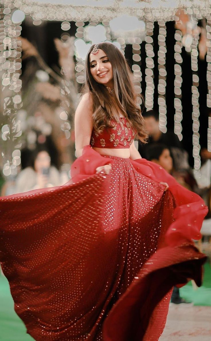 a woman in a red dress is dancing on the street with lights around her and smiling at the camera