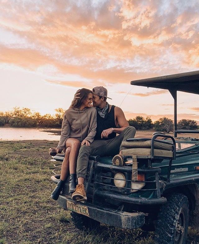 a man and woman sitting on the back of a truck in front of a lake