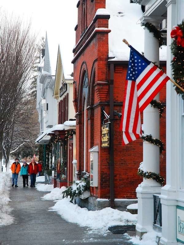 people walking down the street in front of buildings with snow on them and an american flag hanging from the building