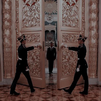 two men in suits and hats are standing near an open door with their hands out