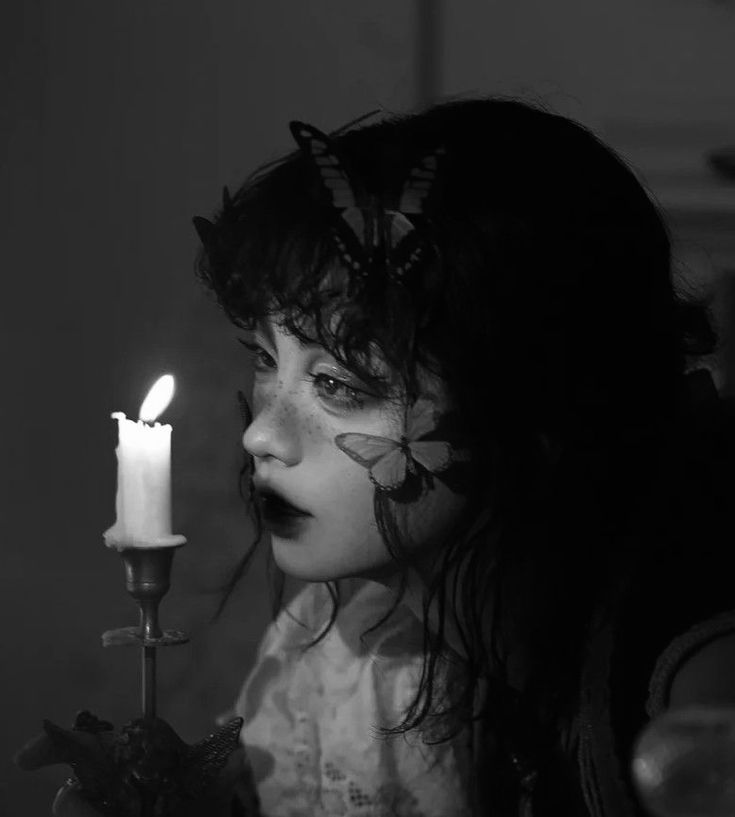 a woman with dark hair and butterfly makeup holding a candle in front of her face