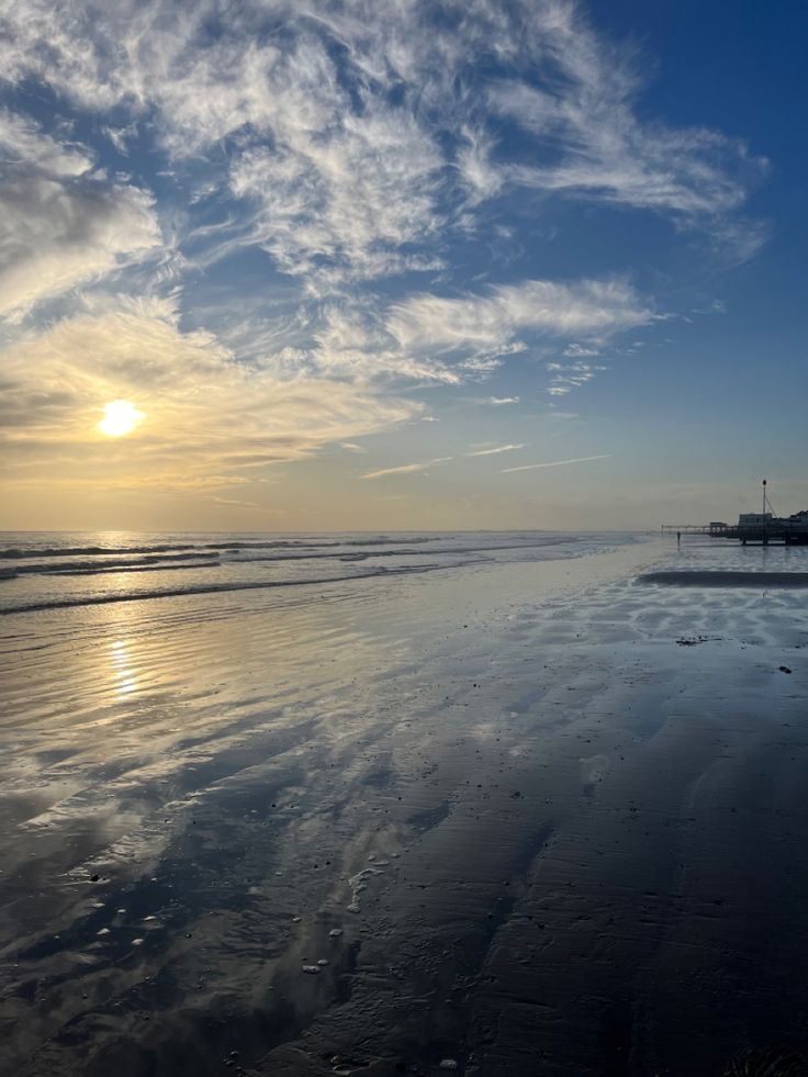 the sun is setting at the beach with some clouds in the sky and sand on the ground