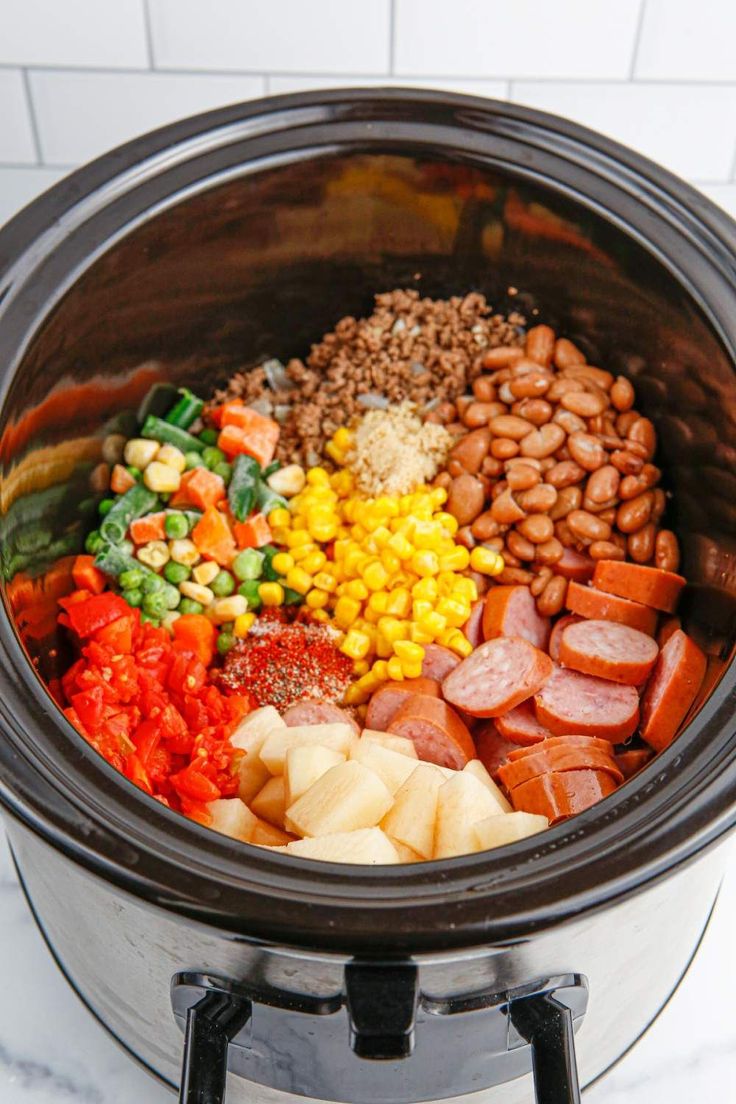 a crock pot filled with beans, corn, carrots and other vegetables