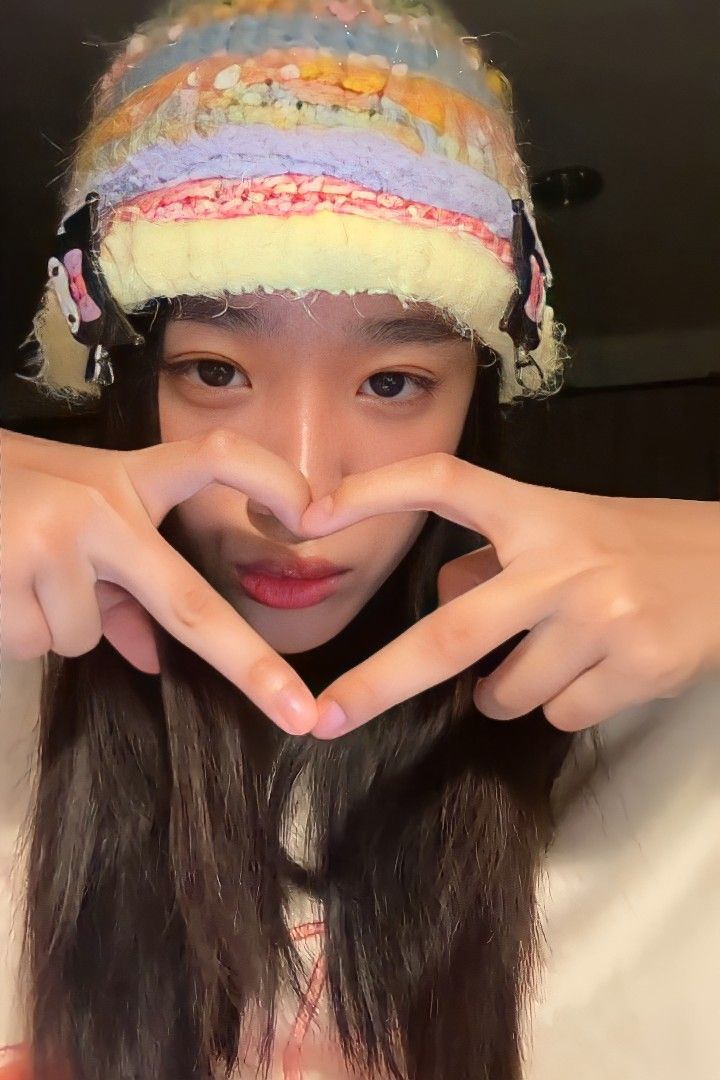 a girl making a heart with her hands and wearing a knitted hat on top of her head