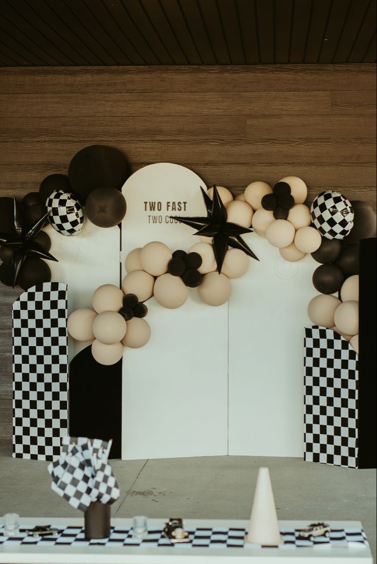 a table topped with balloons and black and white checkered paper decorations on top of it