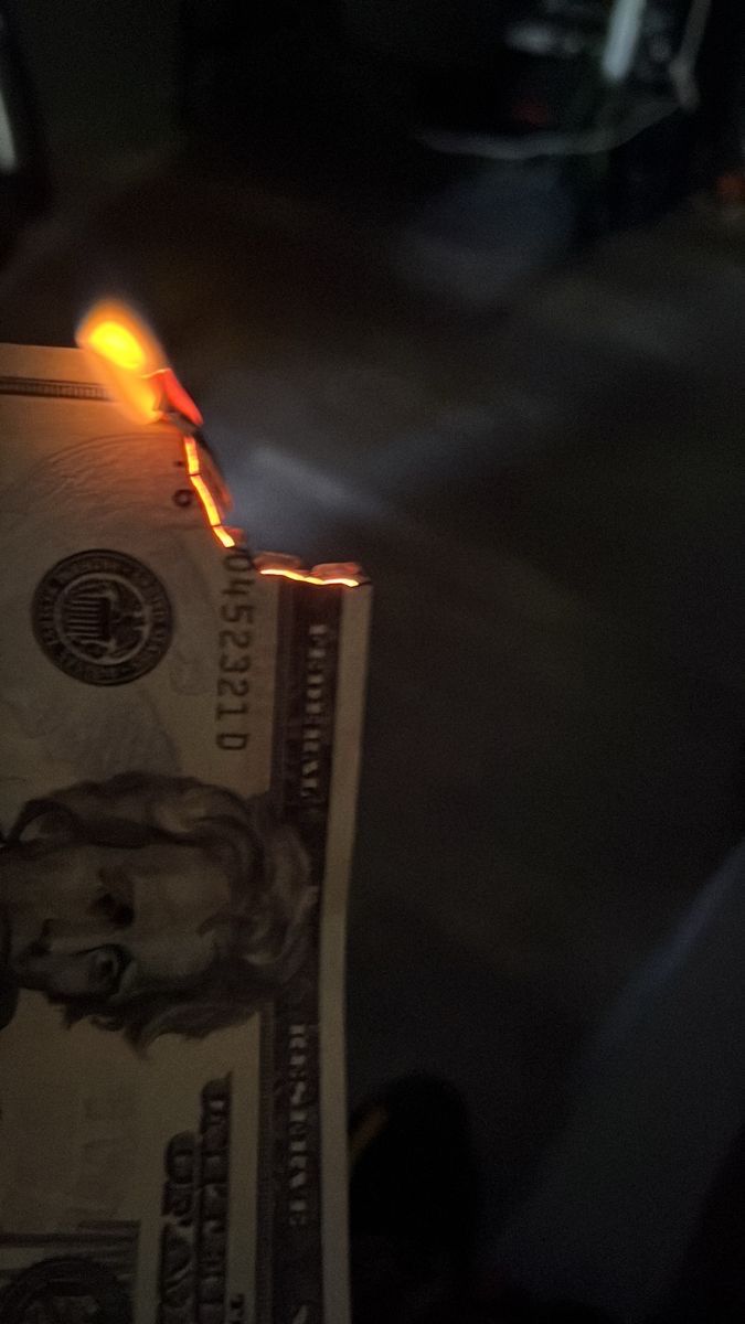 a lit lighter on top of a one dollar bill