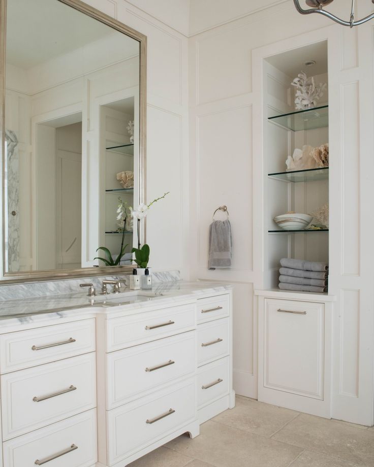 a bathroom with white cabinets and marble counter tops, along with a large mirror on the wall