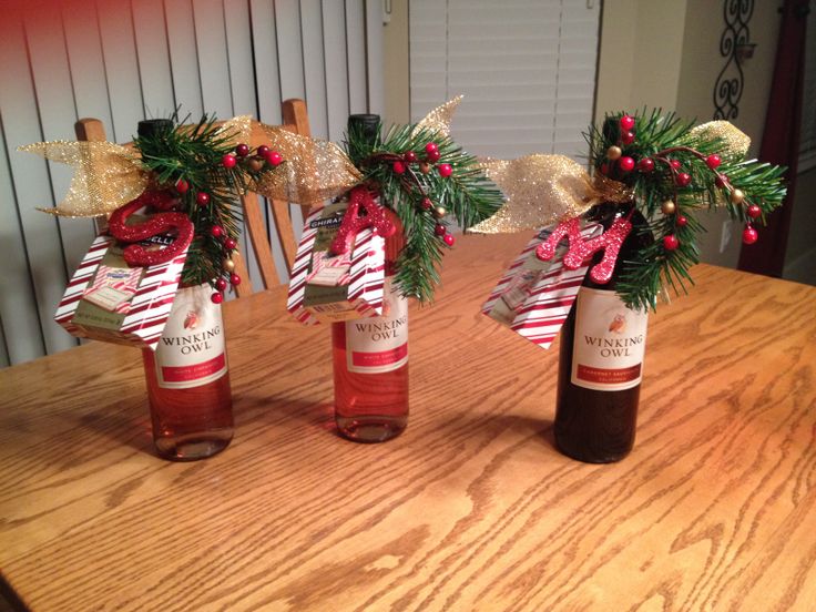 three wine bottles decorated with bows and candy canes, sitting on a wooden table