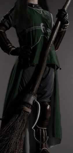 a man dressed in medieval clothing holding a broom and wearing a green outfit with white writing on it