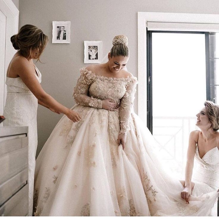 two women in wedding gowns are looking at the bride's dress while another woman looks on