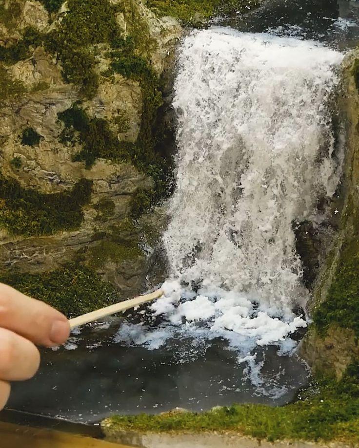 a person holding a toothbrush in front of a waterfall with moss growing on it