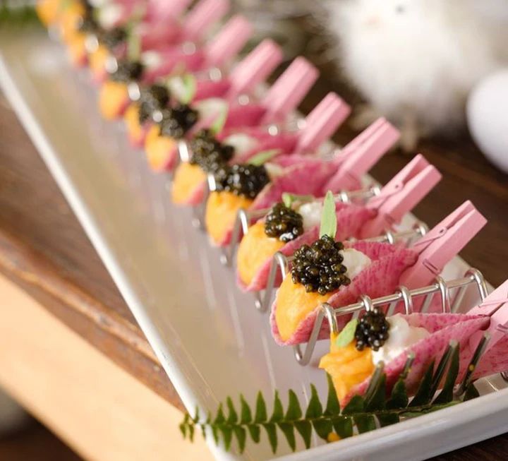 small appetizers are lined up on a white tray with green leaves and flowers