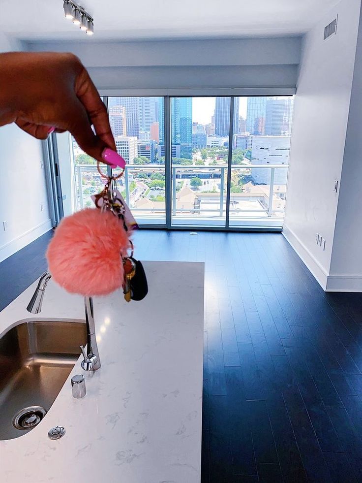 a hand is holding a pink pom - pom keychain in front of a kitchen sink