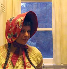 a woman with braids wearing a red hat and yellow dress in front of a window