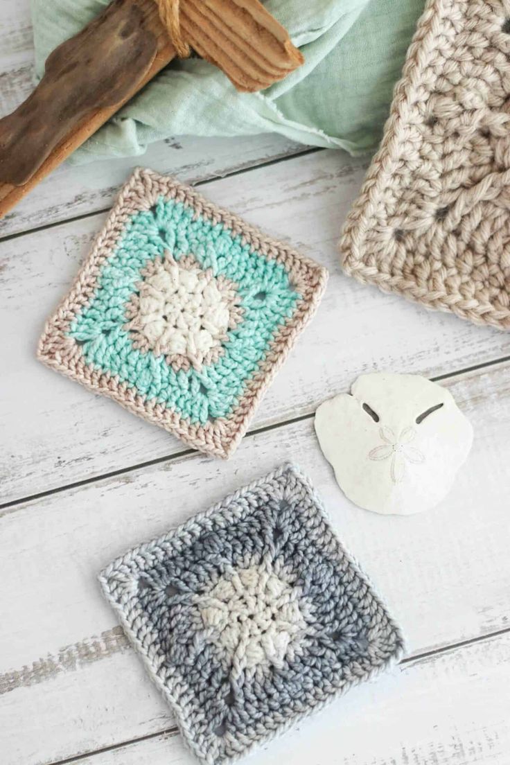 three crocheted squares sitting on top of a white wooden floor next to a piece of wood