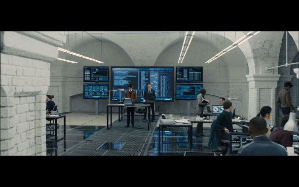 a group of people standing around tables in a room with multiple screens on the wall