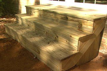 a wooden porch with steps leading up to the front door and side window in the background