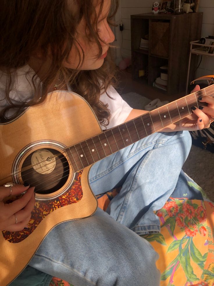 a woman sitting on the floor playing an acoustic guitar