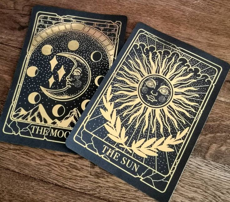 two tarot cards sitting on top of a wooden table with the sun and moon