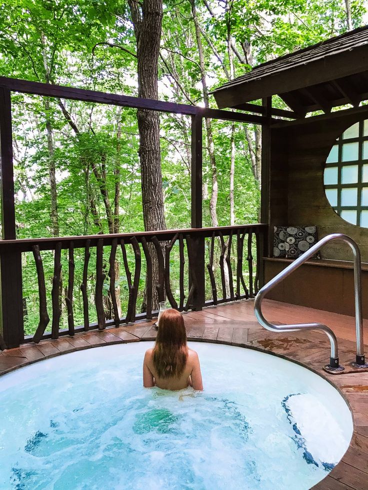 a woman sitting in a large hot tub on top of a deck next to trees