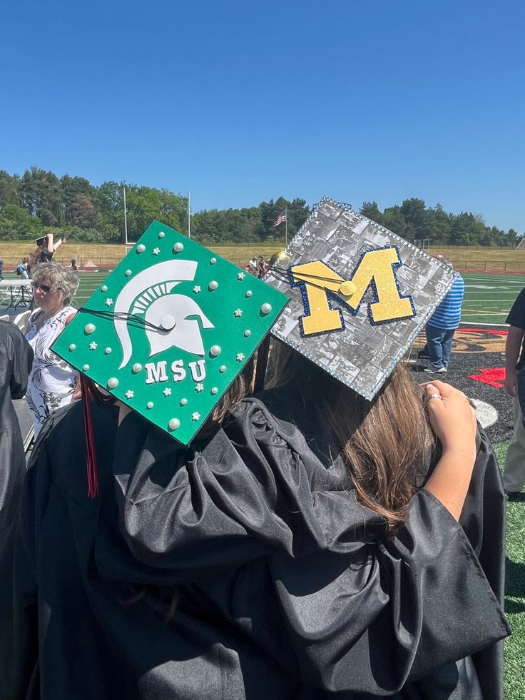 graduates in caps and gowns stand at the end of a football field while others look on