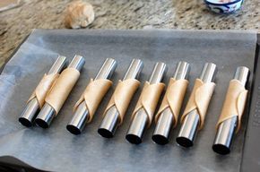 six stainless steel kitchen utensils are lined up on a baking sheet next to a coffee mug