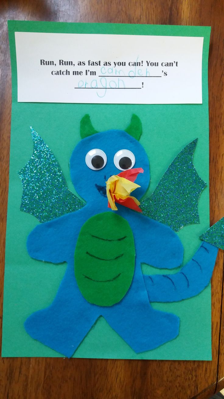 a paper cut out of a blue monster with green wings and a yellow fish in its mouth