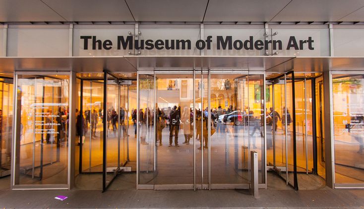 the museum of modern art is reflected in its glass doors as people walk through it