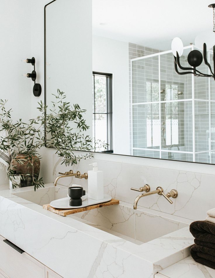 a white bathroom with marble counter tops and gold faucets, black chandelier