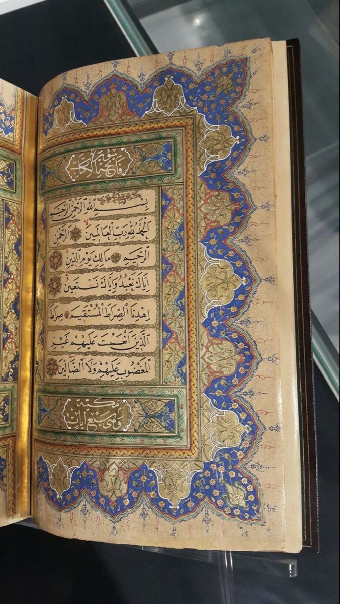 an open book with arabic writing on the pages and gold trimmings, sitting on top of a glass table