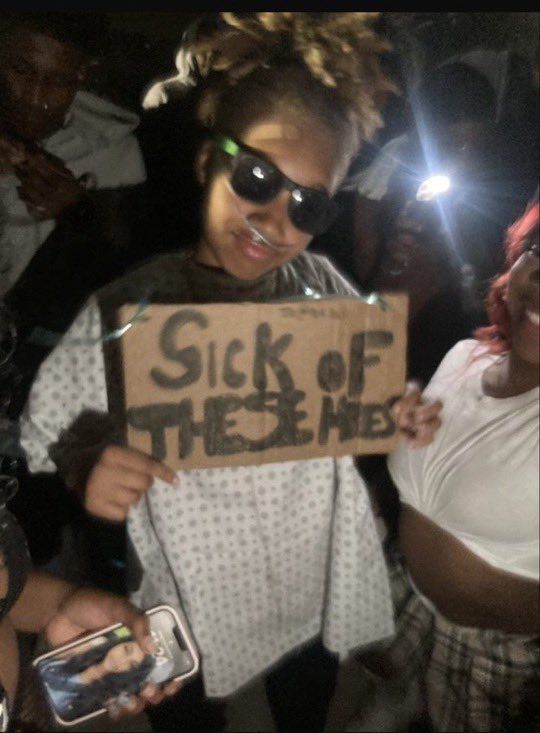 a woman holding a sign that says sick of there he is in front of her