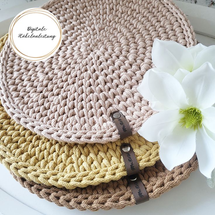 three crocheted round placemats on top of each other with a white flower