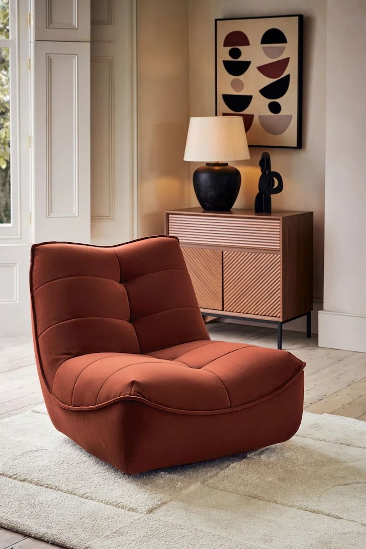 an orange chair sitting on top of a rug in front of a dresser and lamp