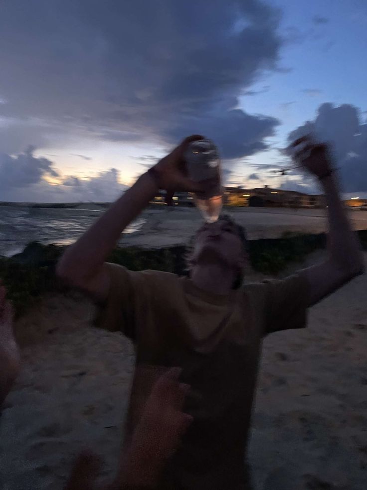 a man standing on top of a sandy beach next to the ocean holding a bottle