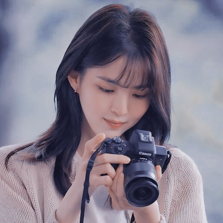 a woman holding a camera up to her face and looking at it with both hands