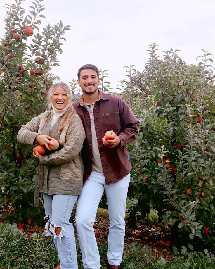 a man and woman holding apples in an apple orchard