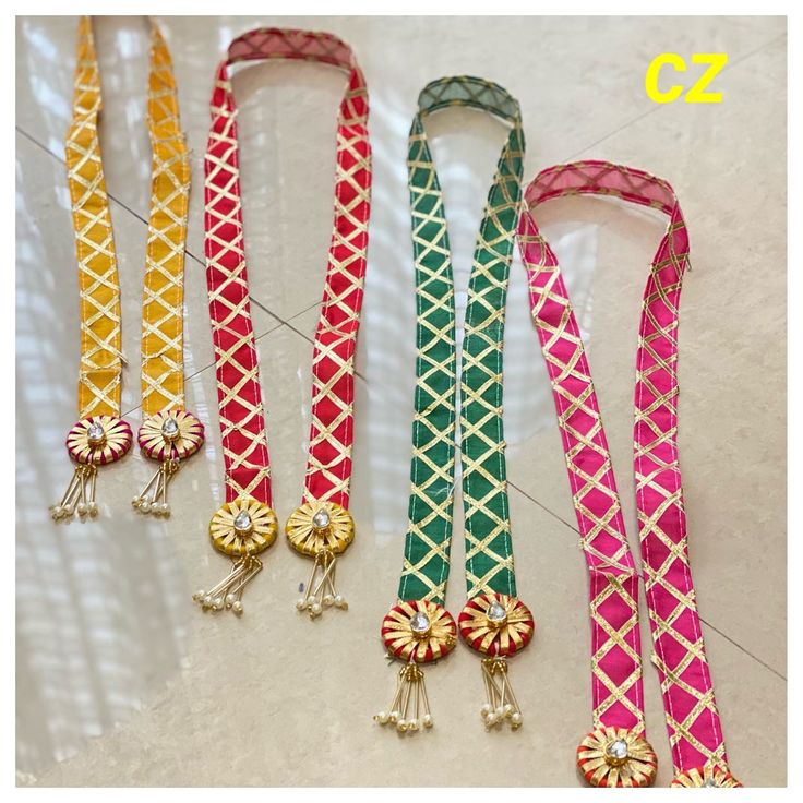 four different colored lanyards are lined up on the floor, one with beads and two with bells