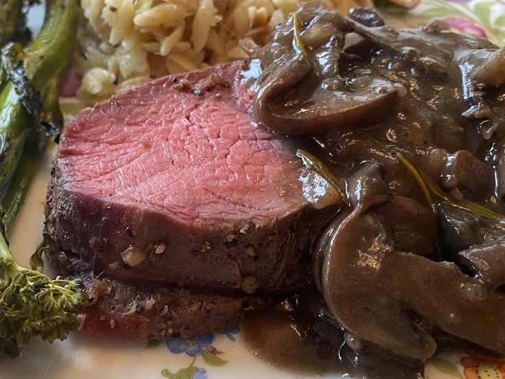 a plate topped with meat and mushrooms next to broccoli on a flowered plate